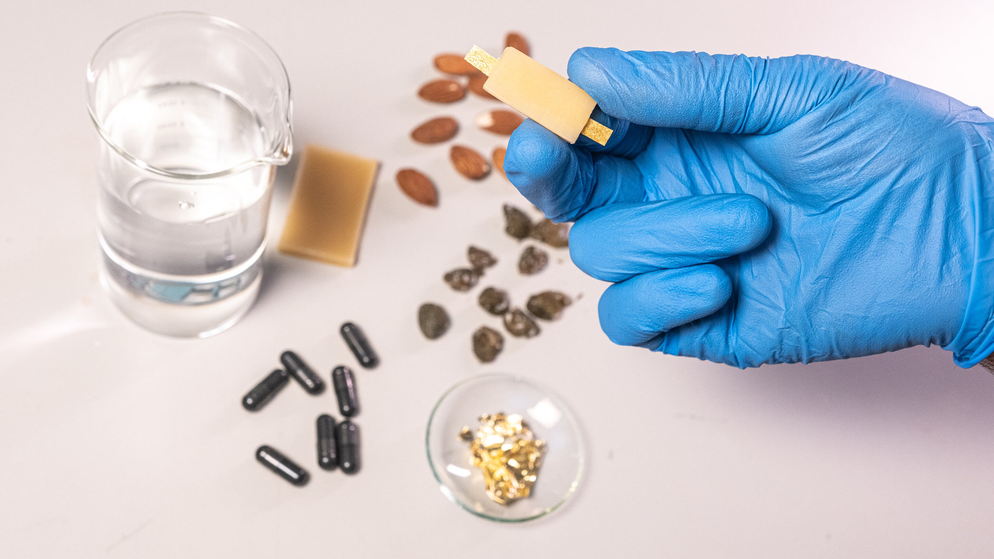 Gloved hand holding up edible battery above its ingredients on table