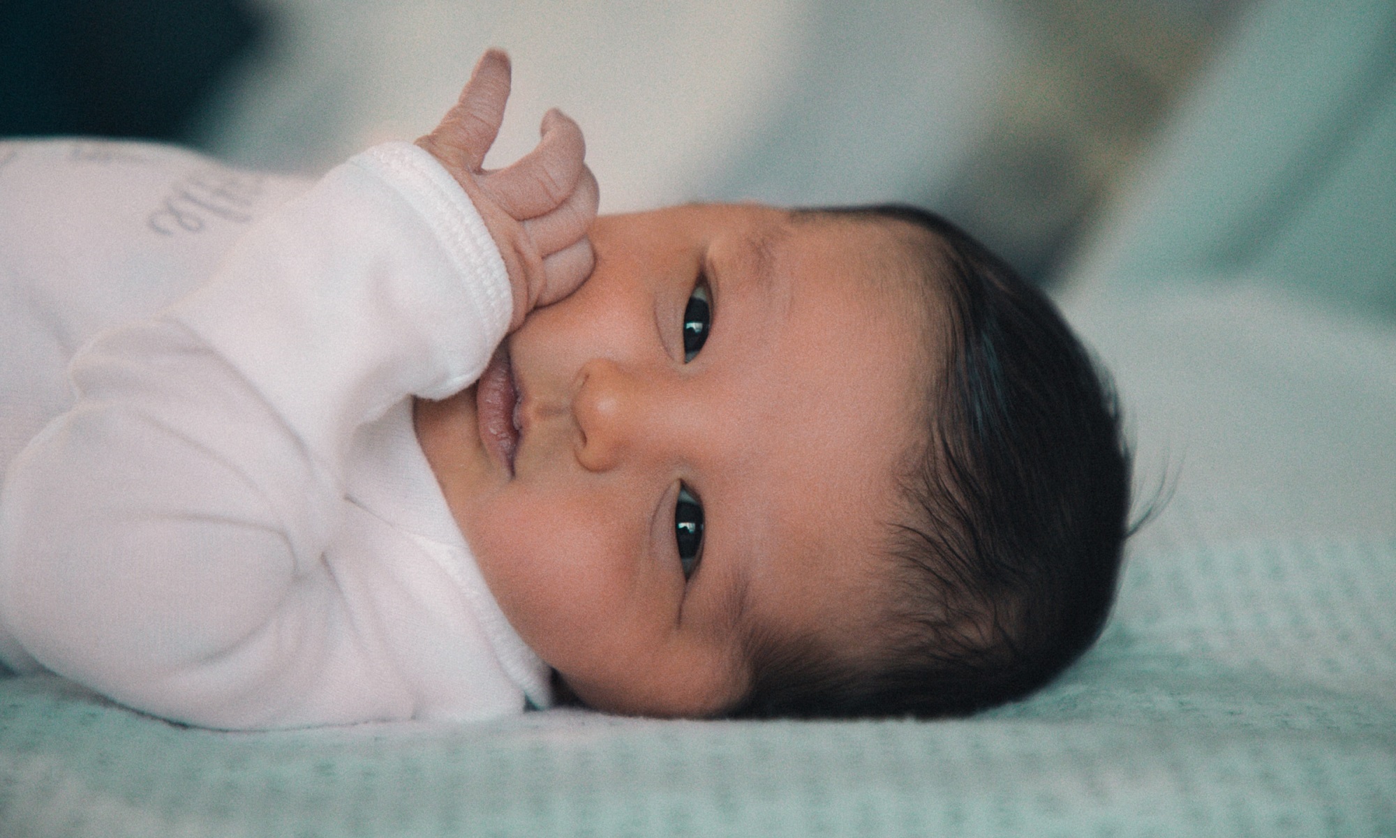 Baby with brown eyes and brown hair laying on their back. The baby is sleeping in a crib, not a bed, to prevent SIDS.