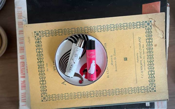  A pink and white Clipper lighter sitting in a dish on top of a pile of books.