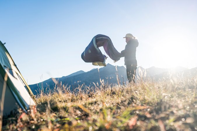 A person shakes out a sleeping bag in the mountains