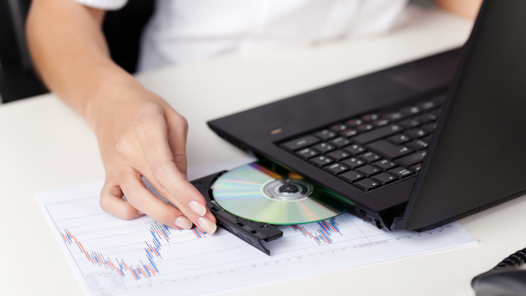 A person putting a DVD or Blu-ray disc into a black laptop, potentially to back it up.