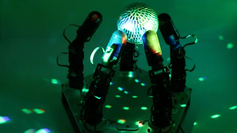 A robotic hand manipulates a reflective disco ball in dim lighting.