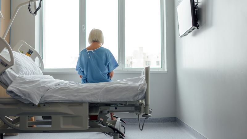 An older woman sits on a hospital bed.