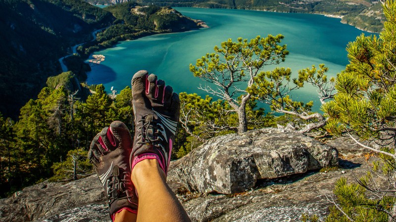 A person wearing barefoot shoes that form around their toes, sitting on a rock overlooking a body of water.