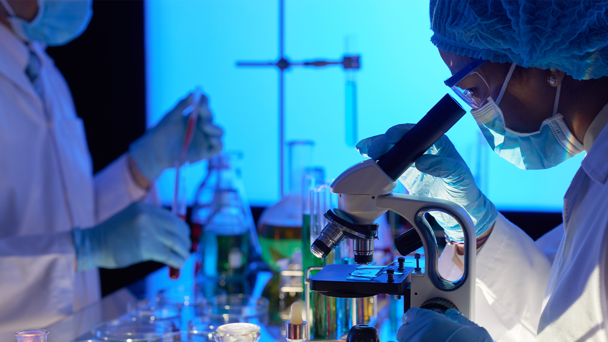 Two doctors performing lab tests, one looking into a microscope and the other using a pipette.