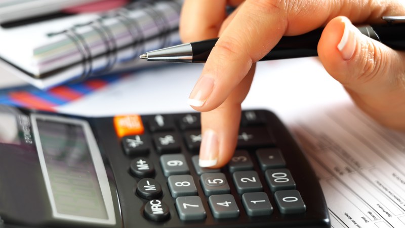 Close up of female hand using calculator atop tax forms.