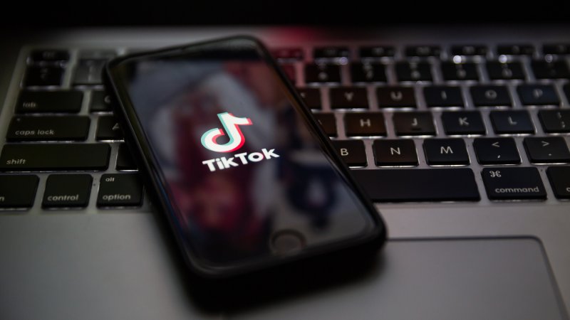 TikTok brand logo on the screen of Apple iPhone on top of laptop keyboard