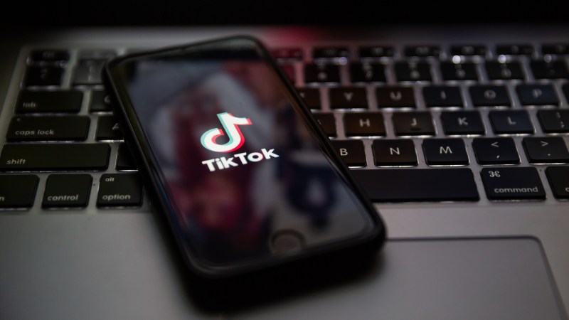 TikTok brand logo on the screen of Apple iPhone on top of laptop keyboard