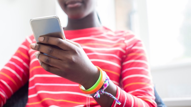 Close Up Of Teenage Girl Wearing Wristbands Using Mobile Phone At Home