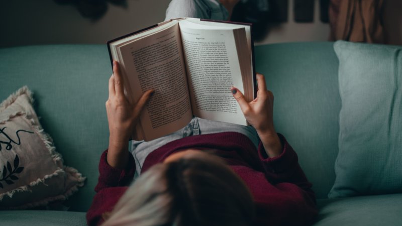 A person sitting on a light green couch reading a book, viewed from above.