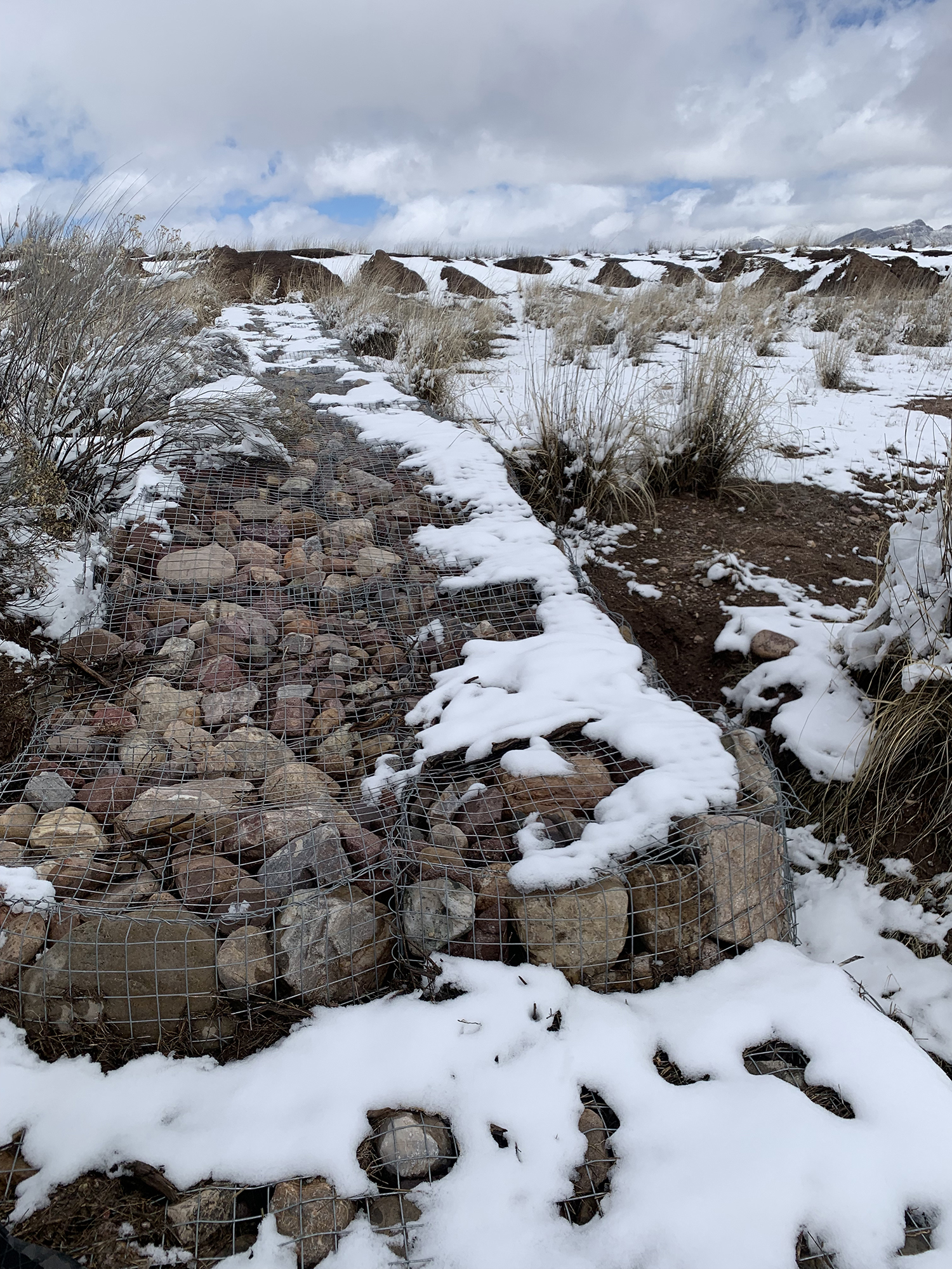 pile of rocks captured in wire fencing with snow on top