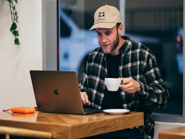 A peson types on an Apple laptop while sipping a coffee