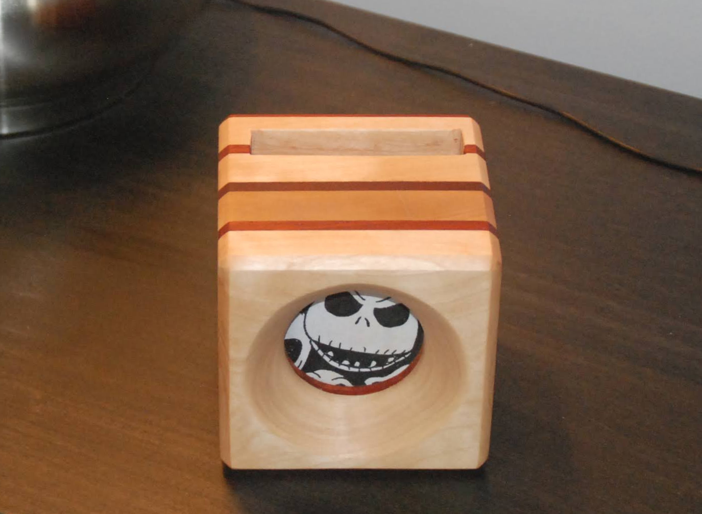 A DIY phone amplifier made out of pale wood, with a Jack Skellington fabric speaker cover and a slot in the top to hold a phone.