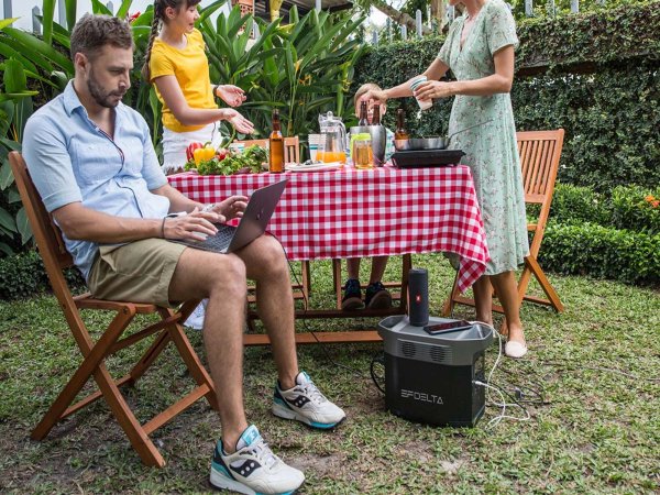 A person sitting outside working on their laptop, which is powered with a portable power station.