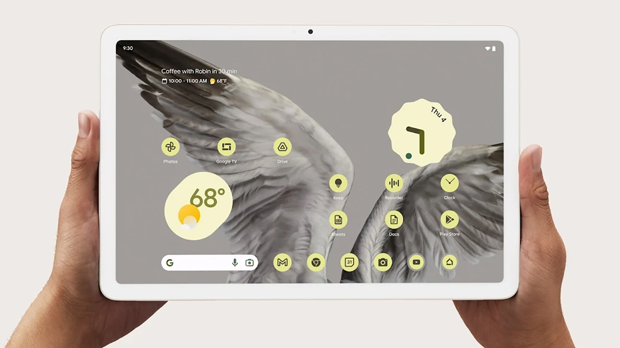 A person holding a Google Pixel Tablet, showing a bird as the wallpaper and various apps on the screen with a clock and weather widget.