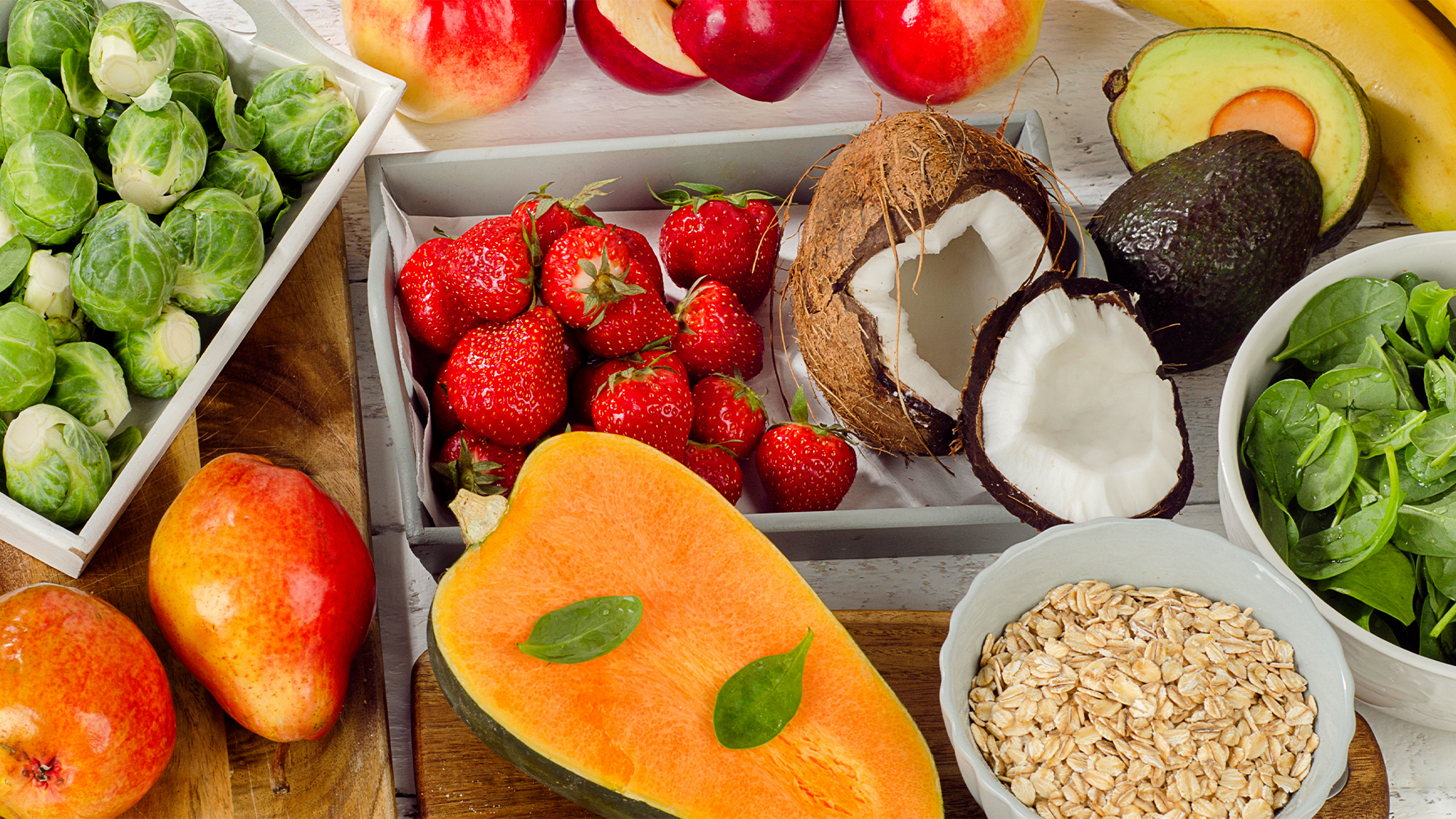 High fiber foods, including coconuts, Brussel sprouts, squash, and spinach on a wooden table.