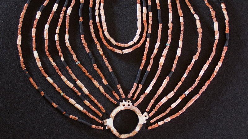 The physical reconstruction of the necklace found in the Neolithic village of Ba’ja in Jordan. It has about 16 strands of beads that meet together in a circle with a gemstone in it and three other strands on top.