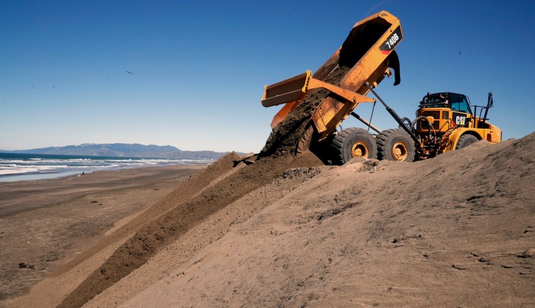 Giant yellow dump truck depositing sand on San Francisco beach because of coastal erosion