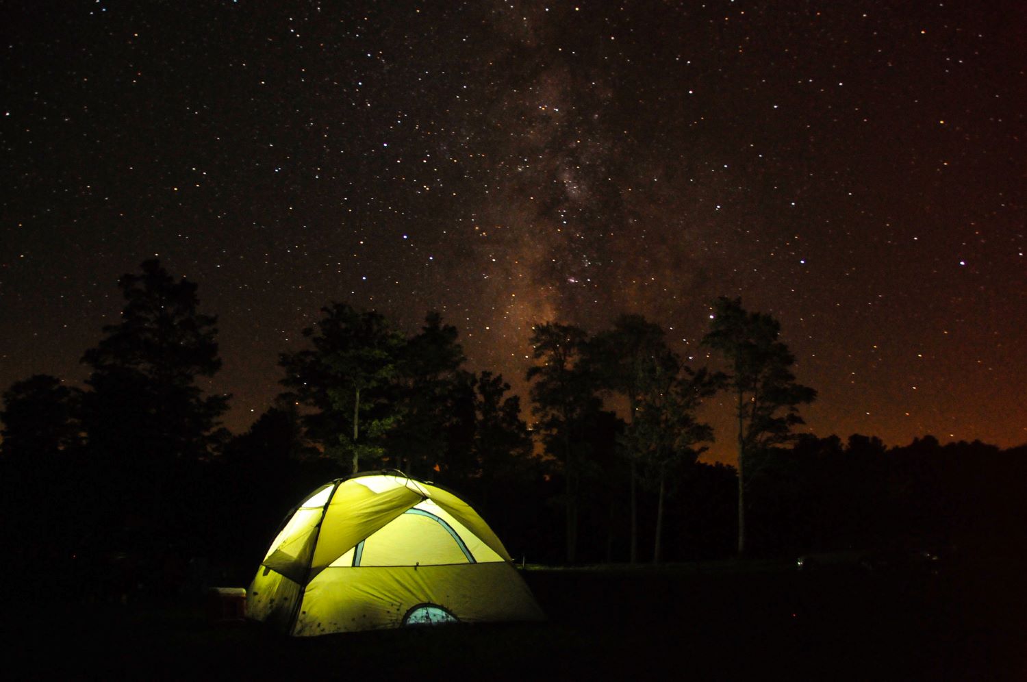 A tent is illuminated beneath the night sky.