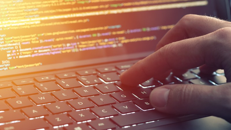 Close-up of hand typing computer coding on laptop screen