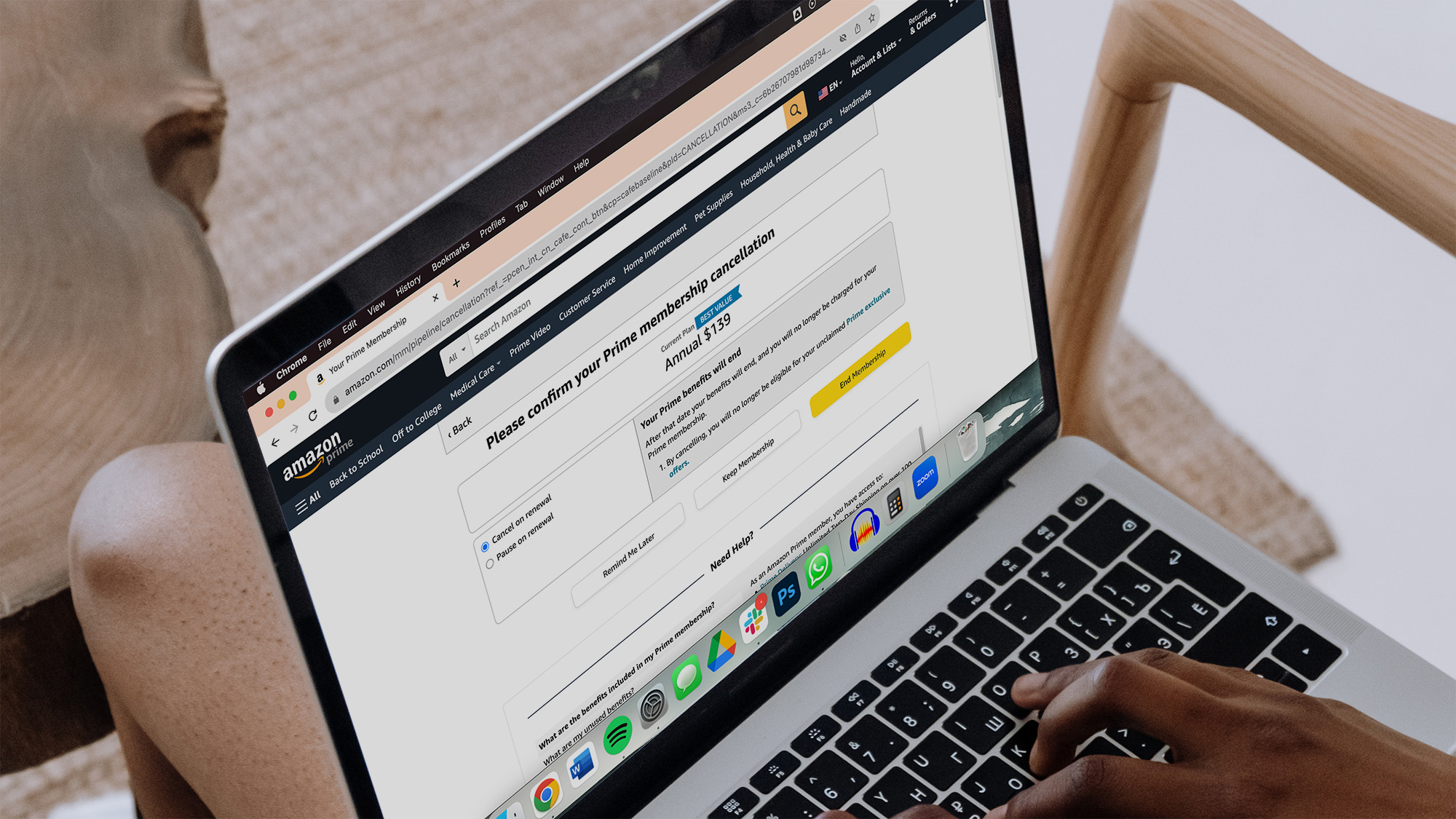 A person sits with their laptop on their legs and Amazon open in their browser to figure out how to cancel Amazon Prime.