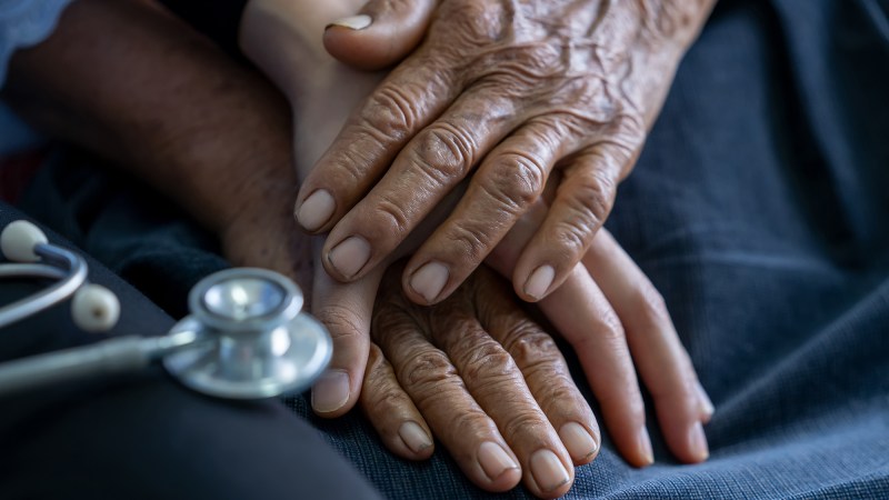 Close up of young nurse holding old man's hands and encourage him.