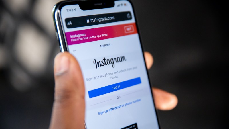 A person's hand holding an iPhone with the Instagram login screen visible.