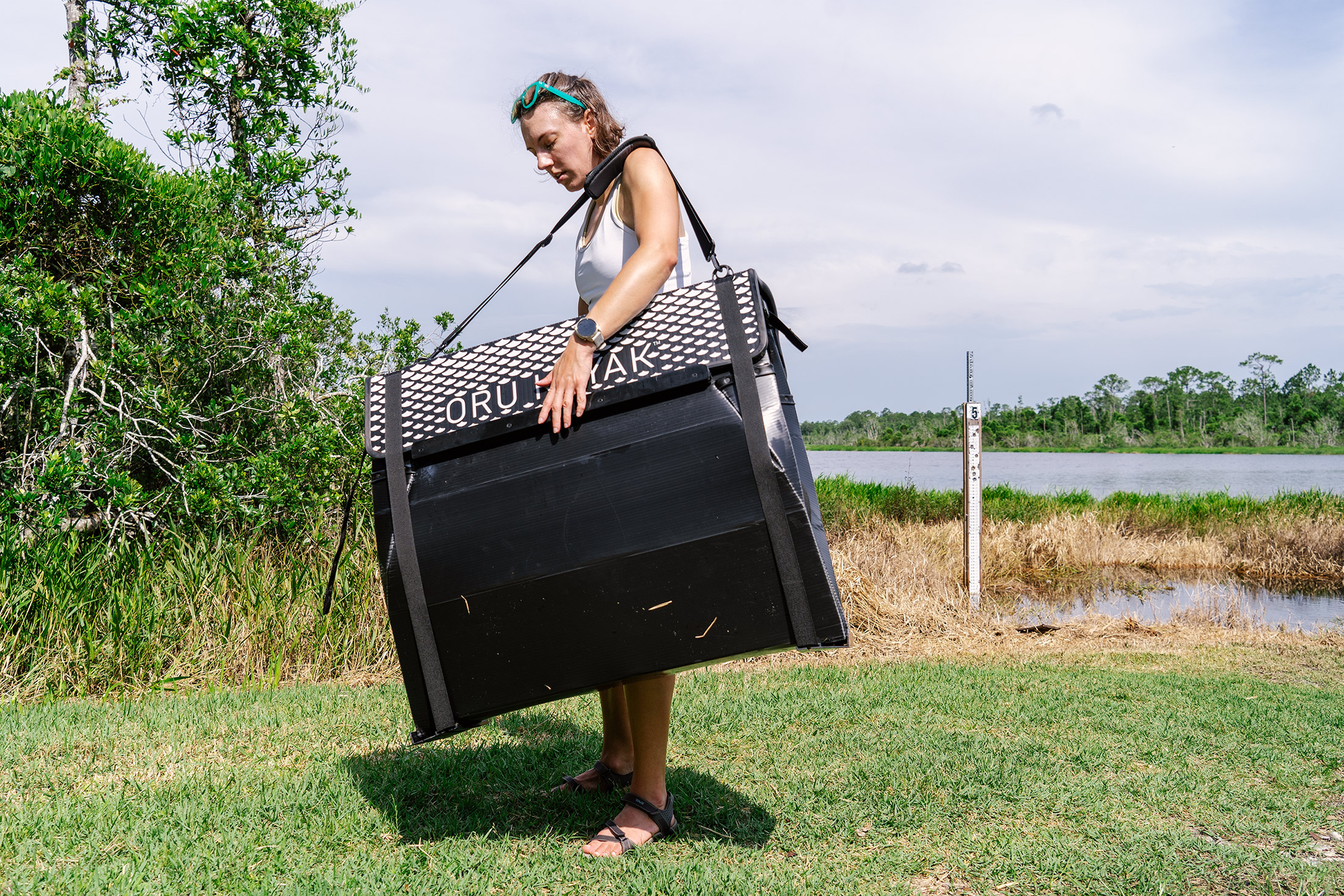 The Oru Beach LT Sport folded down and carried by a woman on a shoreline.