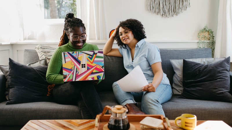 Two women sitting on a couch using a Windows computer.