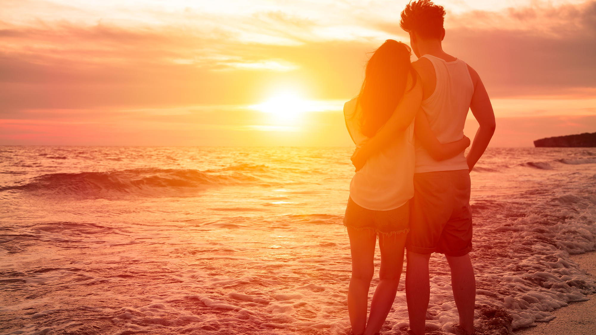 A couple standing on the beach in warm sunlight.