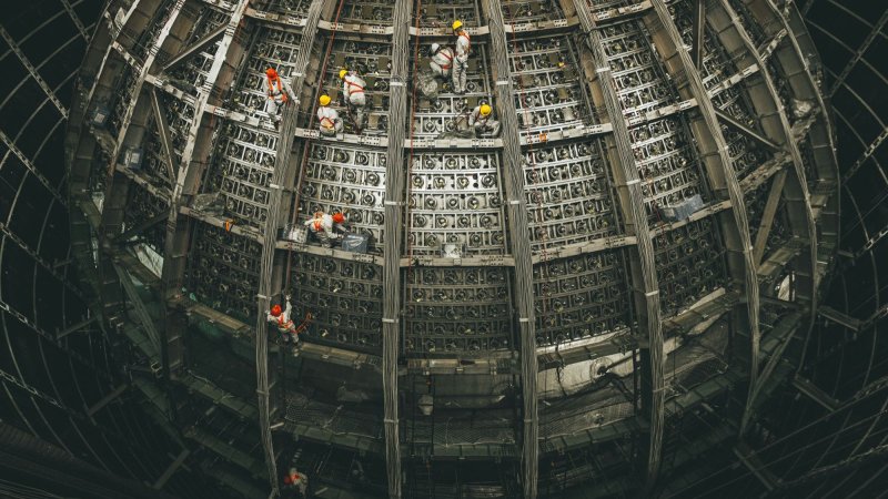 A metal sphere under construction as workers climb over it.