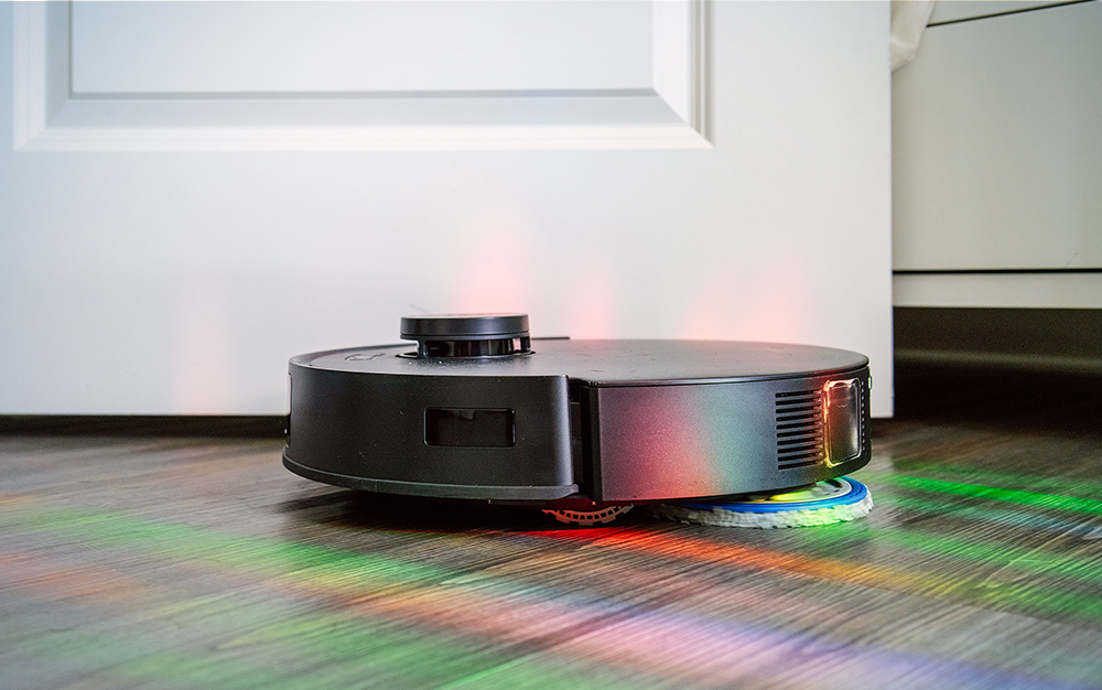 Black robot vacuum mopping a hardwood floor covering in rainbow light