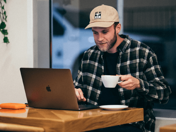 A person drinking a cup of coffee working on their laptop