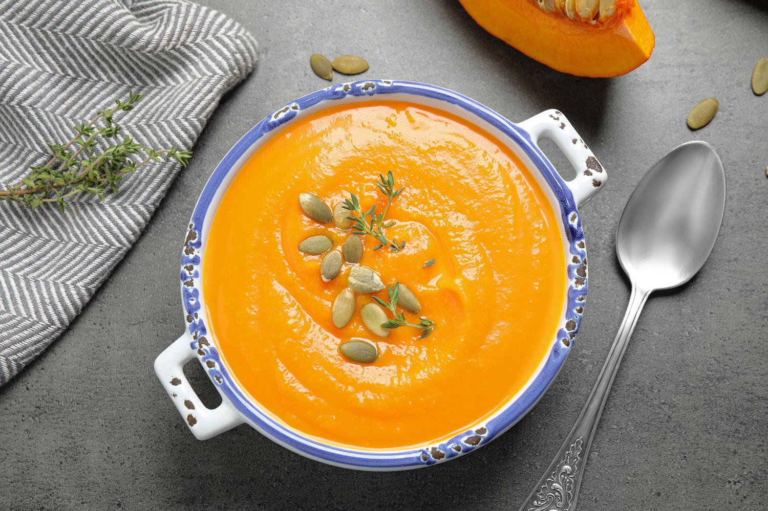 Pumpkin soup topped with pumpkin seeds and herbs in a blue bowl