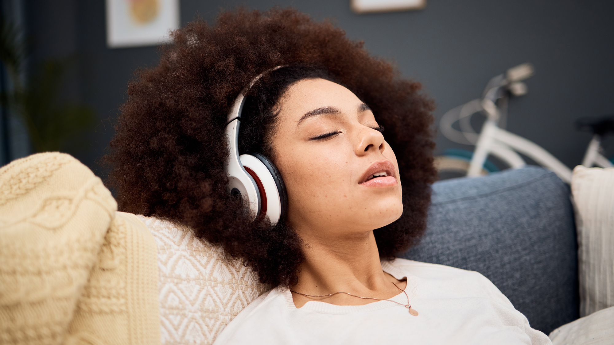 A woman wearing over the ear headphones leans her head back and closes her eyes.