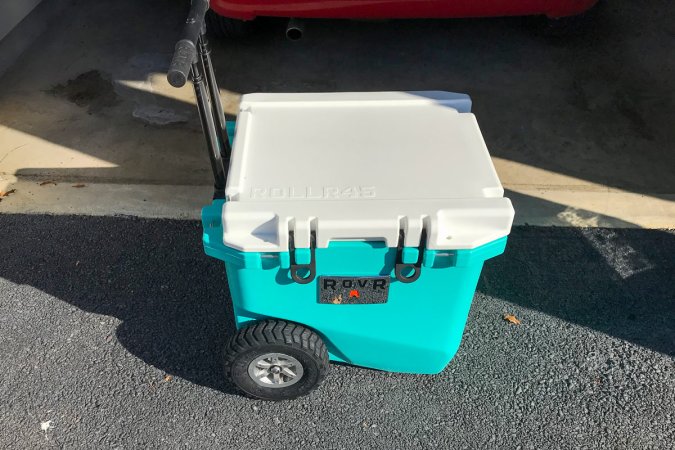  A blue RovR RollR 45 Wheeled Cooler sits on a driveway.