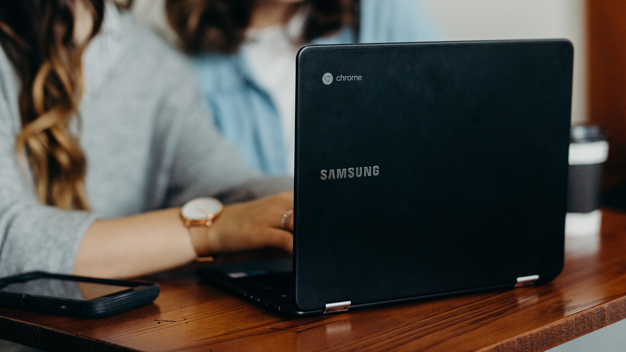 Person sat on a wooden desk working on a open Chromebook laptop