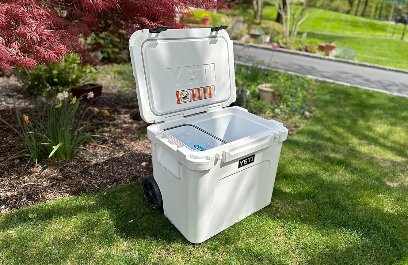 White Yeti Roadie cooler on wheels with its lid open sitting on a very green lawn in the sunshine.