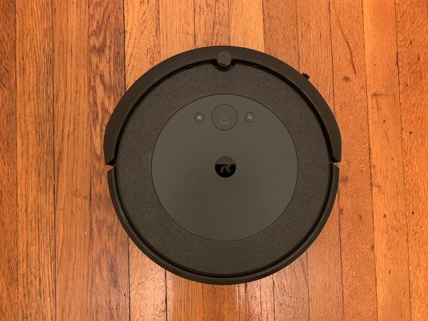  A round black iRobot Roomba i4 against a wooden floor.