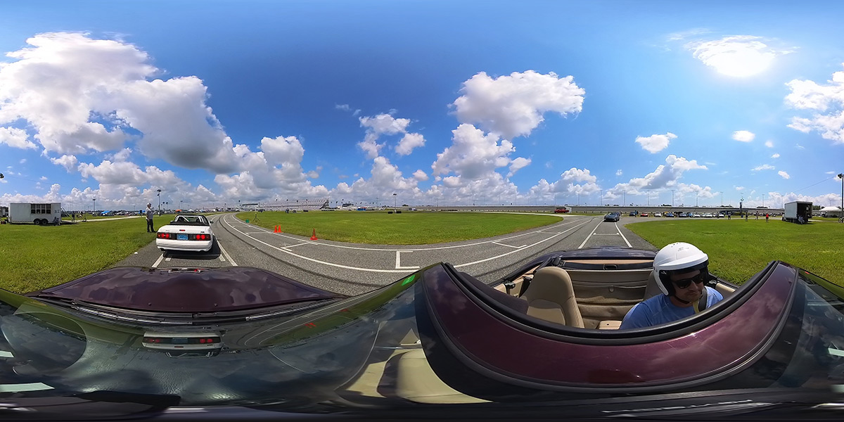 A man sits in a convertible on a track with a blue sky around him.