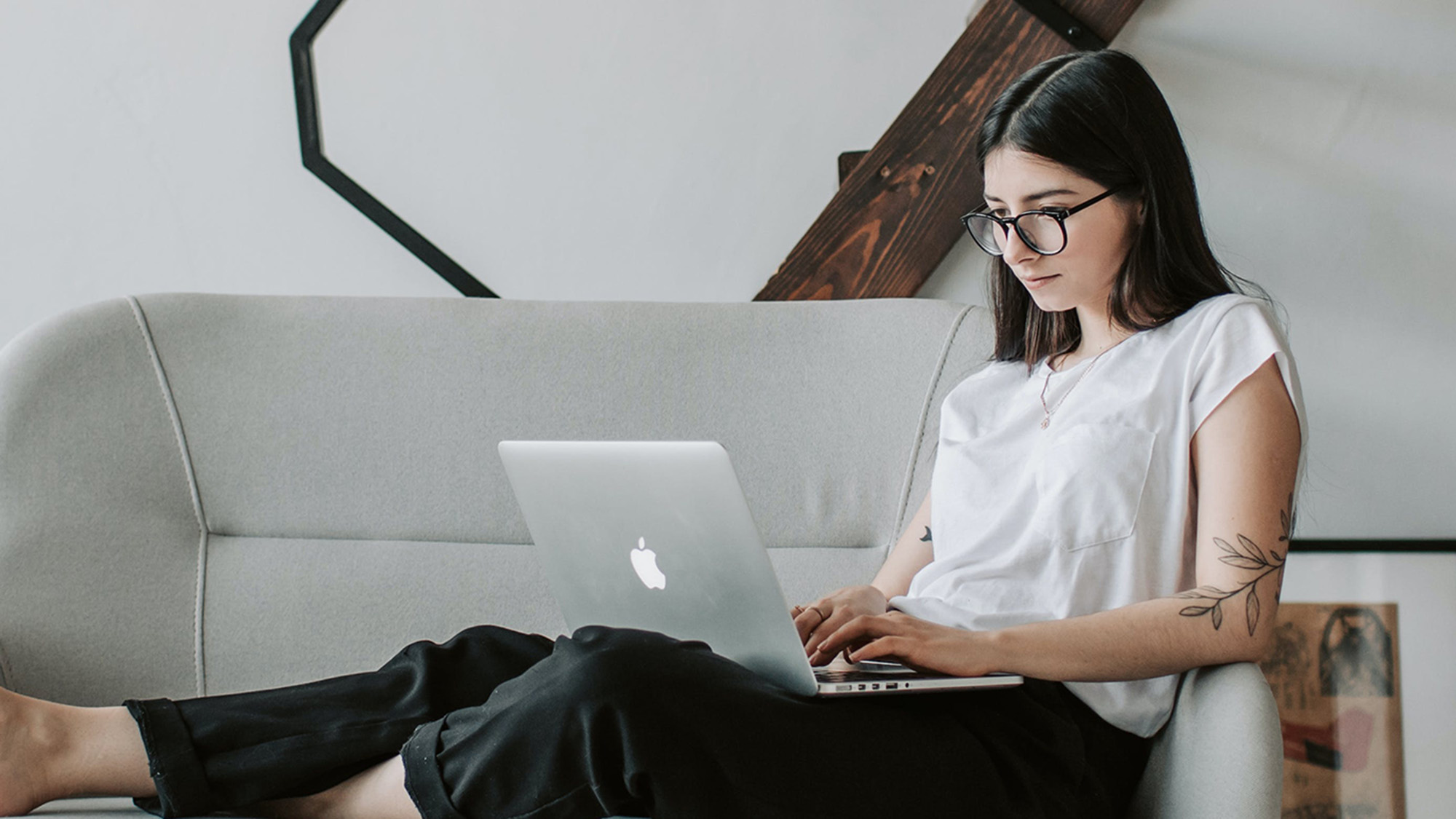 Person laying on a gray couch in a living room, working on a MacBook