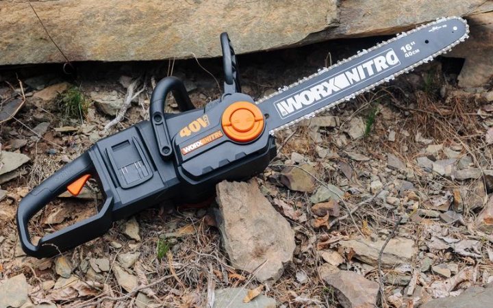  A black Worx Nitro chainsaw set in front of some rocks against some brown leaves.