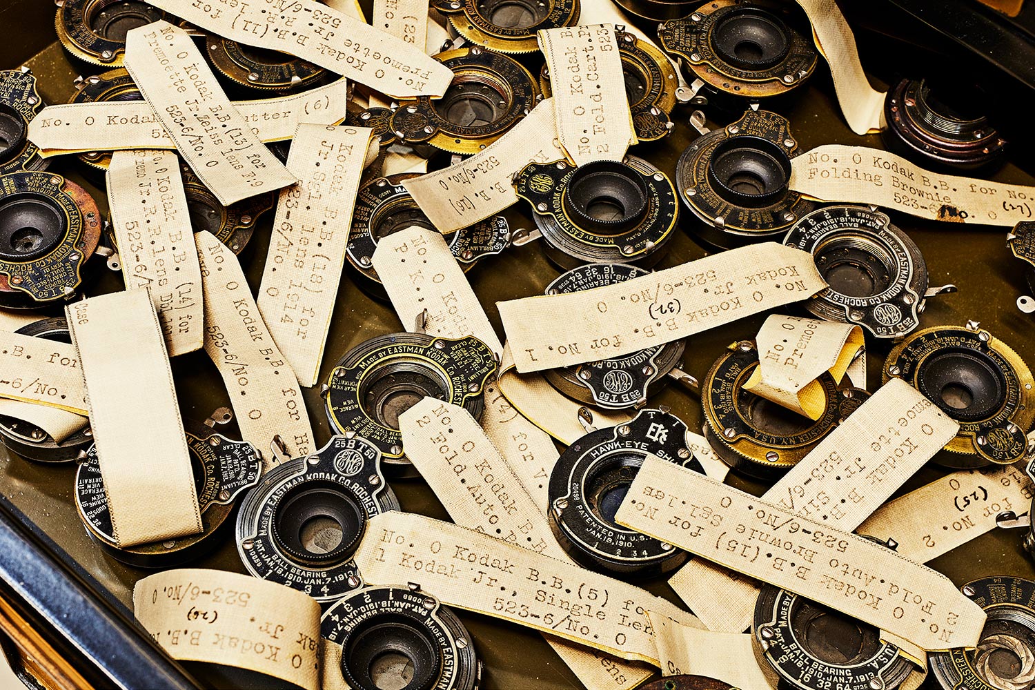 inside of a drawer containing a pile of various shutter mechanisms from many Kodak cameras made a century ago