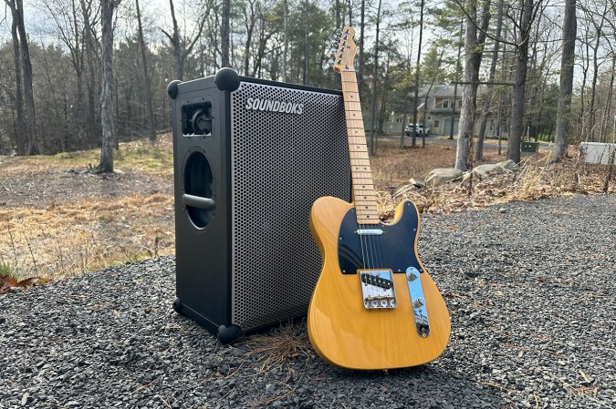  Black Soundboks 4 outdoors speaker with an orange Fender guitar on a gravel patio