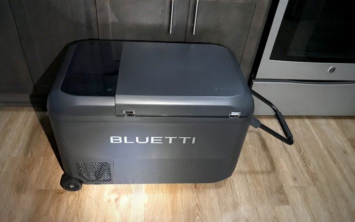  Shiny BLUETTI MultiCooler in front of a full-sized refrigerator on a glossy wood kitchen floor