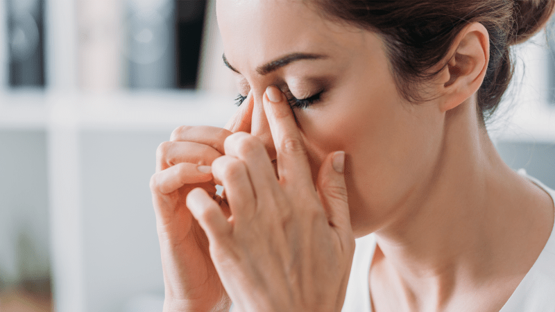 A woman in pain puts her hands up to her nosed with her eyes closed.