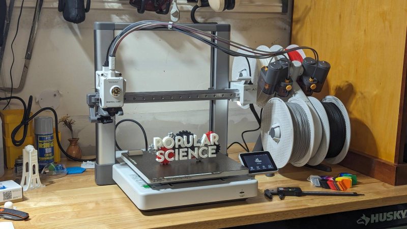 Bambu Labs A1 combo 3D printer on a work bench with a finished print on its bed