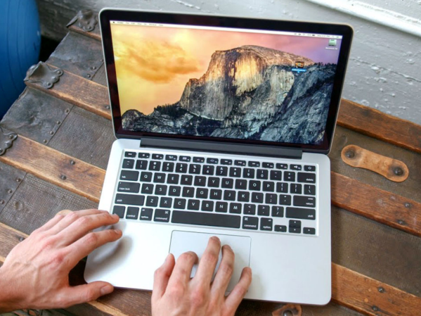 A person working on a refurbished Macbook Pro on a wooden table.