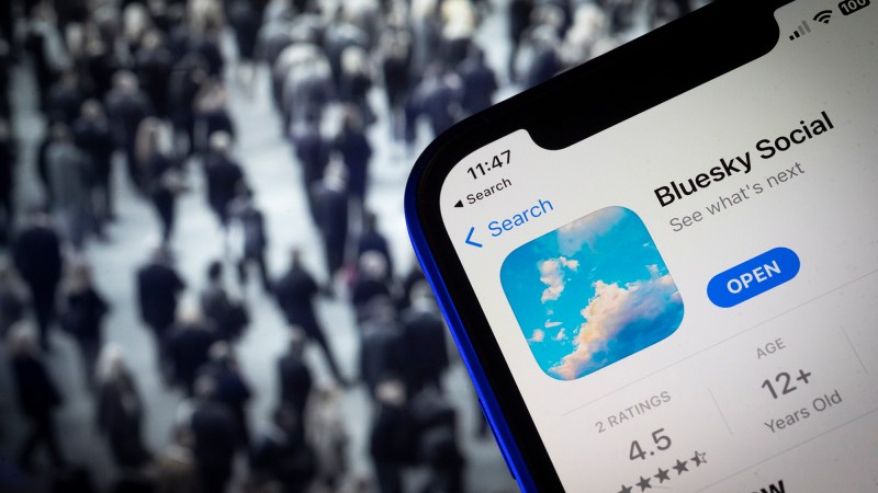 Bluesky app logo on phone superimposed atop crowd of people