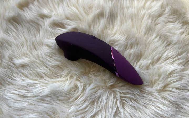  A purple Womanizer Next sex toy on a white fuzzy carpet.